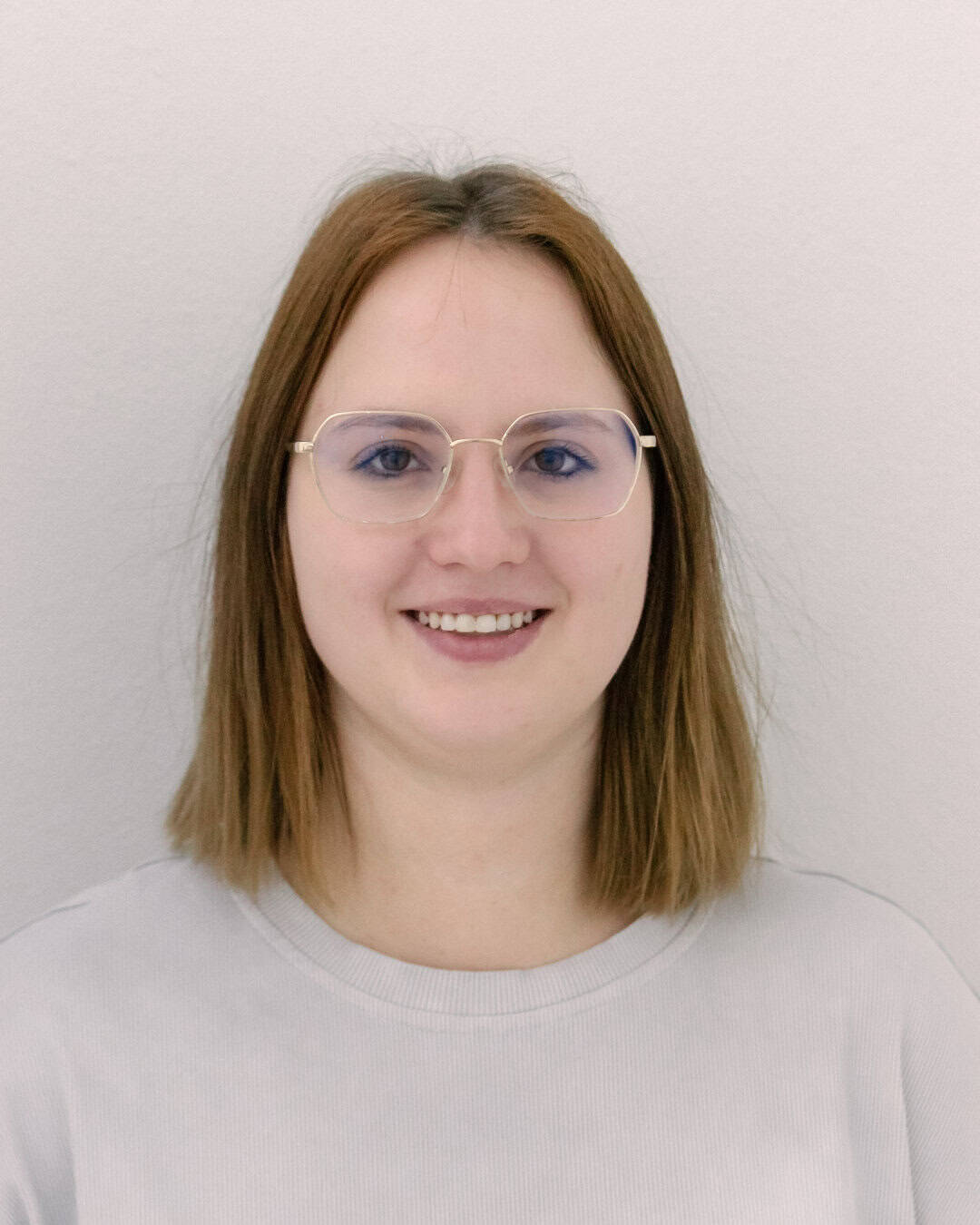 Lebensnahe, freundliche Frau mit Brille vor neutralem Hintergrund.