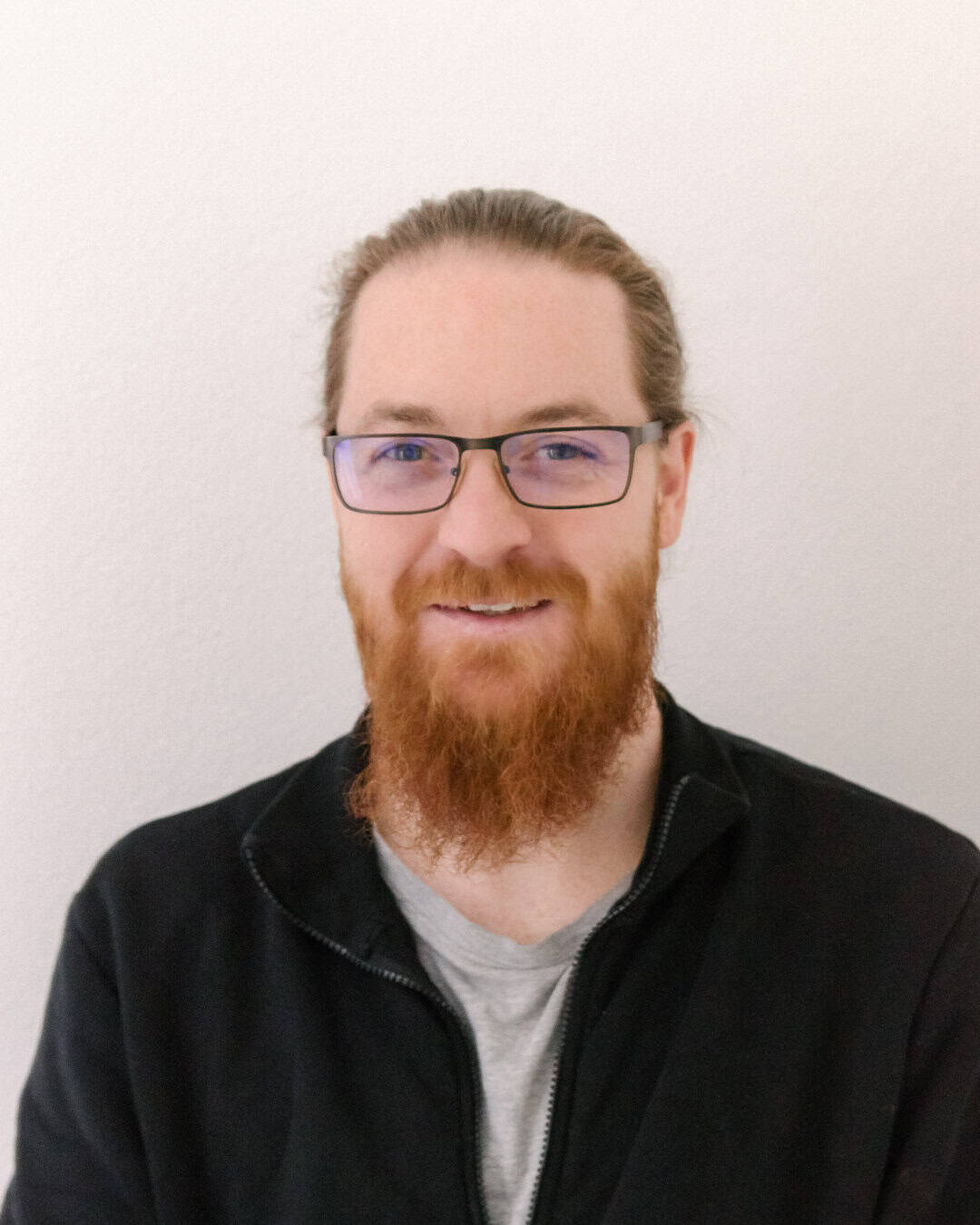 Sehr glücklicher Mitarbeiter mit Brille und rotem Haar vor neutralem Hintergrund.